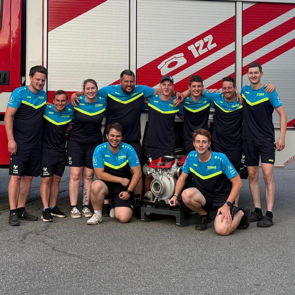 Feuerwehrteam mit Tragkraftspritze vor einem roten Feuerwehrauto mit der Nummer 122